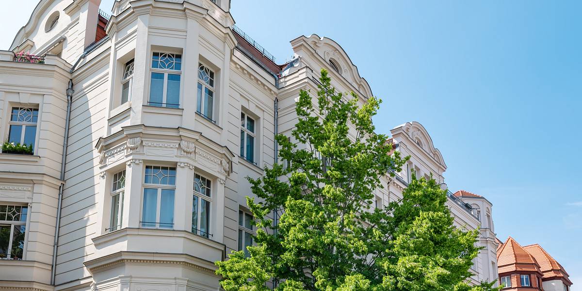 Historisches Mehrfamilienhaus mit reich verzierter Fassade unter blauem Himmel – Symbol für den städtischen Immobilienmarkt.