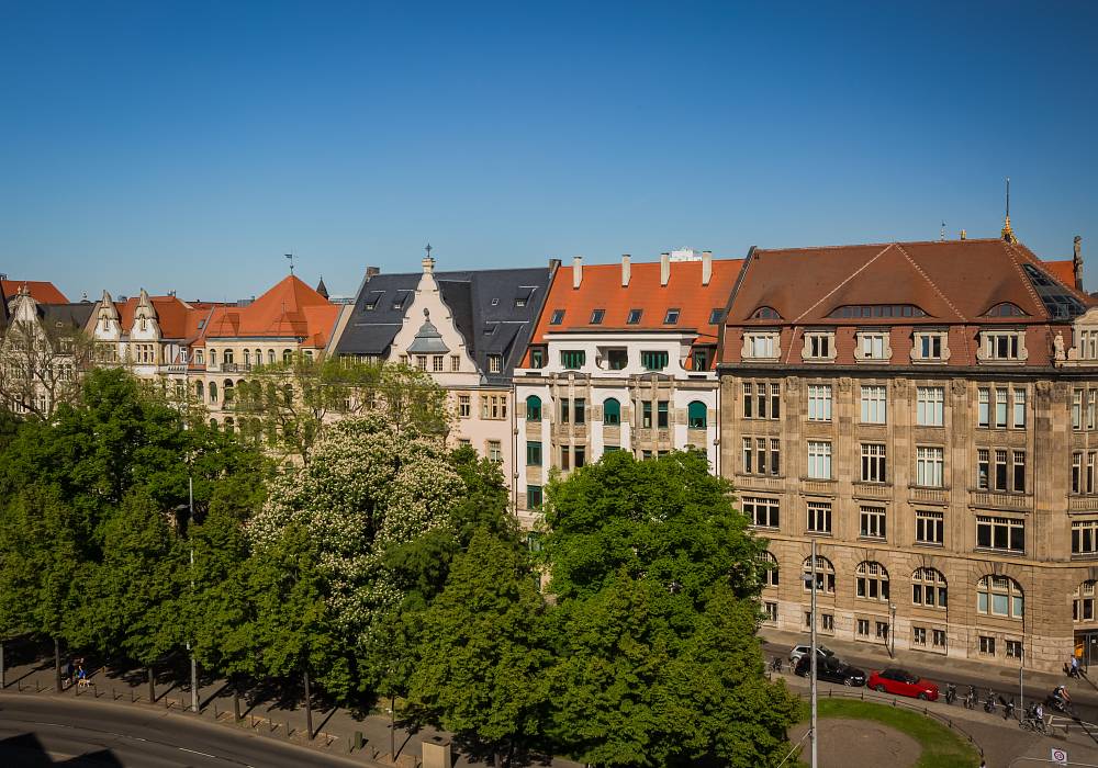 Historische Mehrfamilienhäuser in Leipzig entlang einer baumbestandenen Straße bei sonnigem Wetter