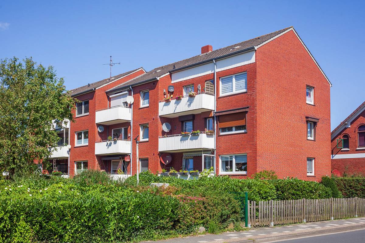 Typisches deutsches Mehrfamilienhaus aus rotem Klinker mit Balkonen und gepflegtem Vorgarten.