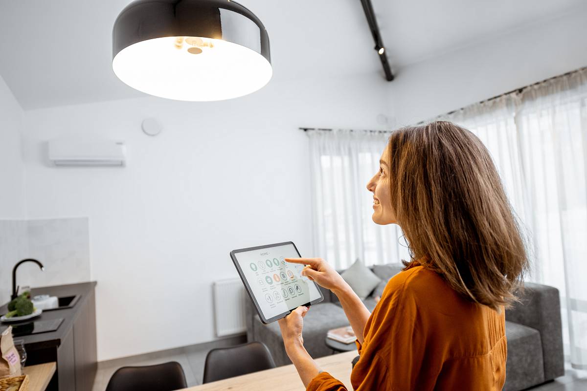 Frau steuert ein modernes Smart-Home-System mit einem Tablet in einem hellen Wohnraum.