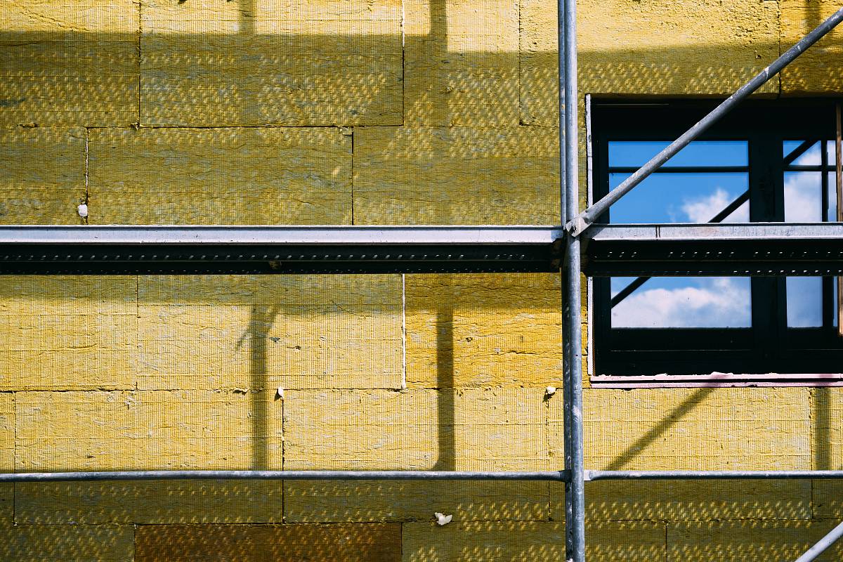 Fassade eines Gebäudes mit gelber Dämmung aus Mineralwolle und Baugerüst – energetische Sanierung durch Wärmedämmung.