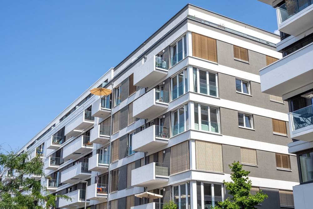 Modernes Mehrfamilienhaus in Berlin mit Balkonen und großen Fenstern bei blauem Himmel.