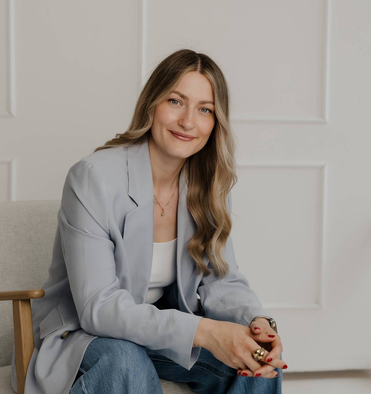 Junge Frau sitzt lächelnd auf einem Stuhl in modernem, hell eingerichtetem Büro.