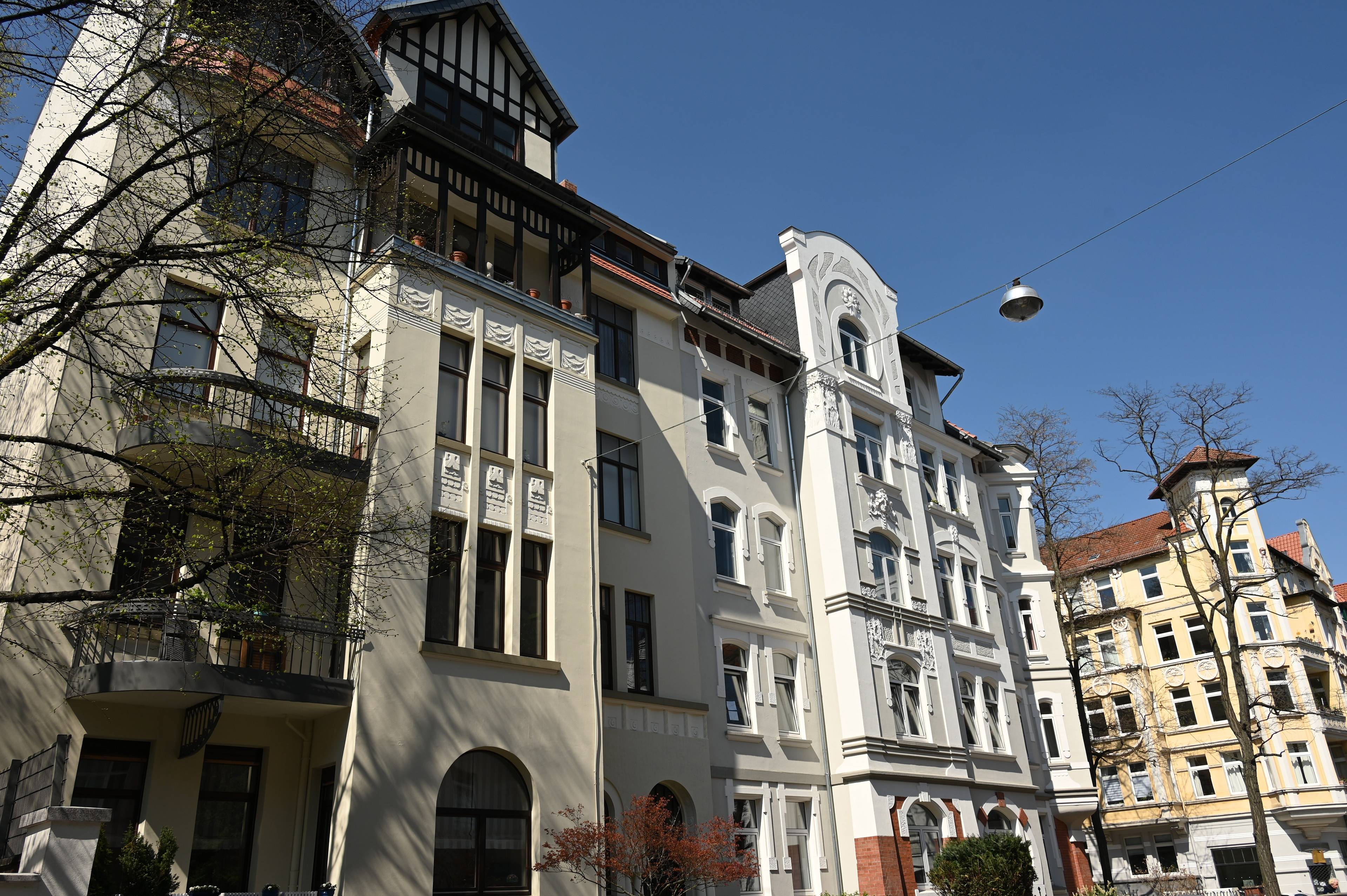 Sanierte Altbaufassaden mit dekorativen Stuckelementen und großen Fenstern in einer Wohnstraße in Hannover bei blauem Himmel.
