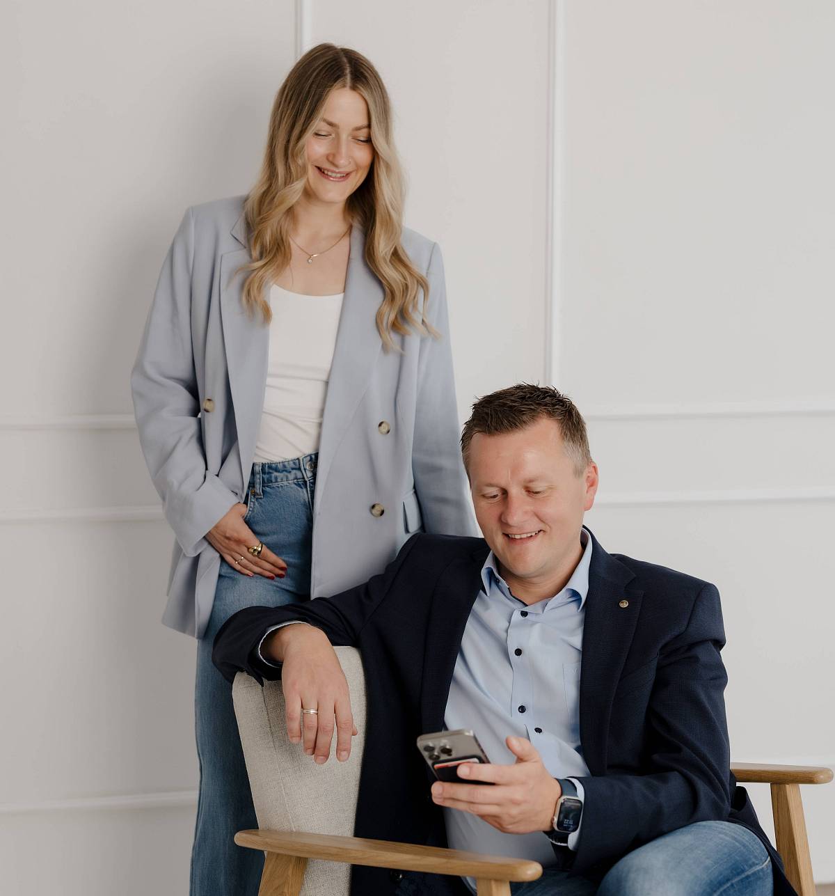 Zwei Immobilienexperten von Peter Vogt Immobilien, lächelnd im Gespräch, der Mann sitzt und schaut auf ein Smartphone, die Frau steht daneben