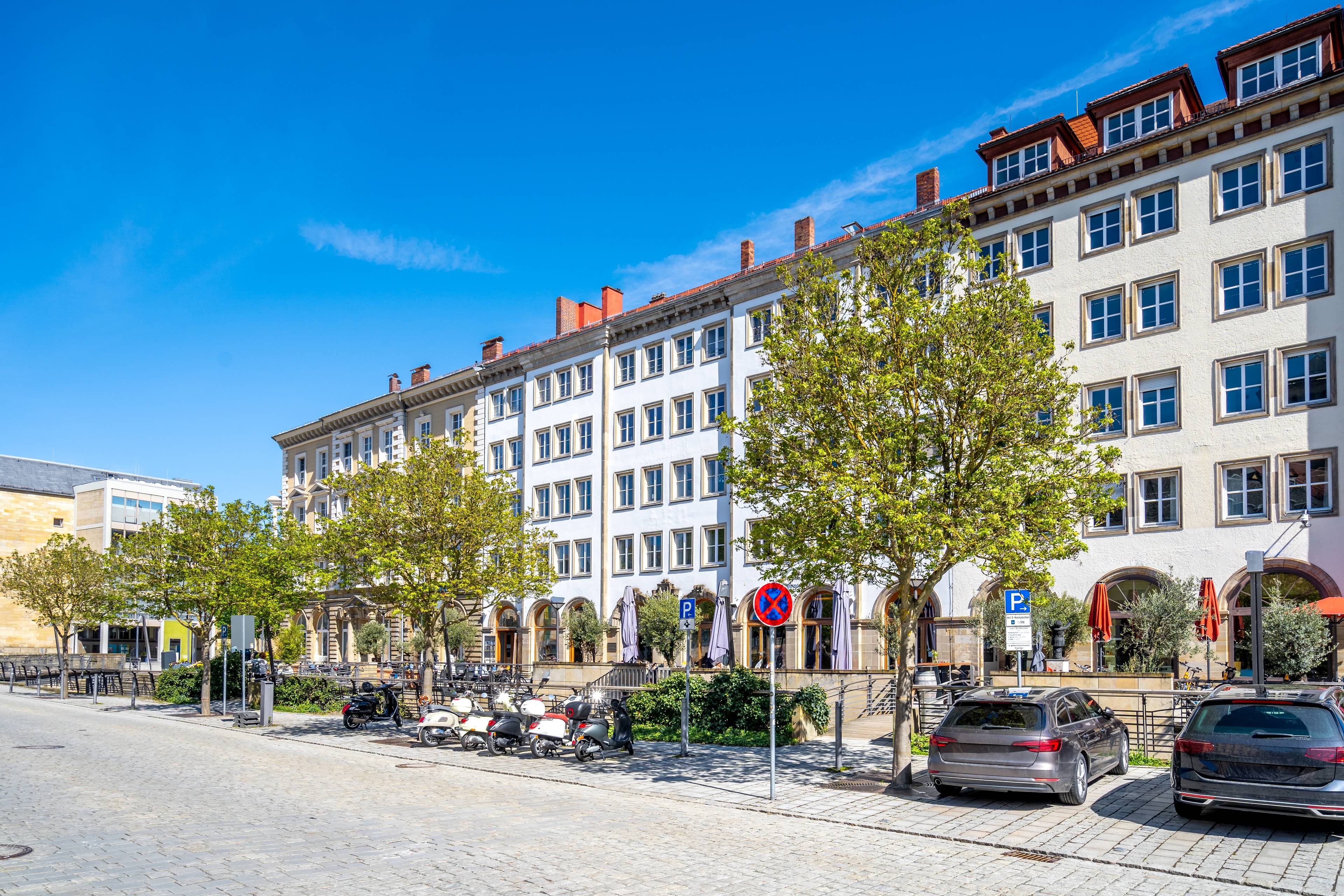 Reihe moderner Mehrfamilienhäuser mit heller Fassade und Bäumen entlang einer ruhigen Straße in Bayreuth.