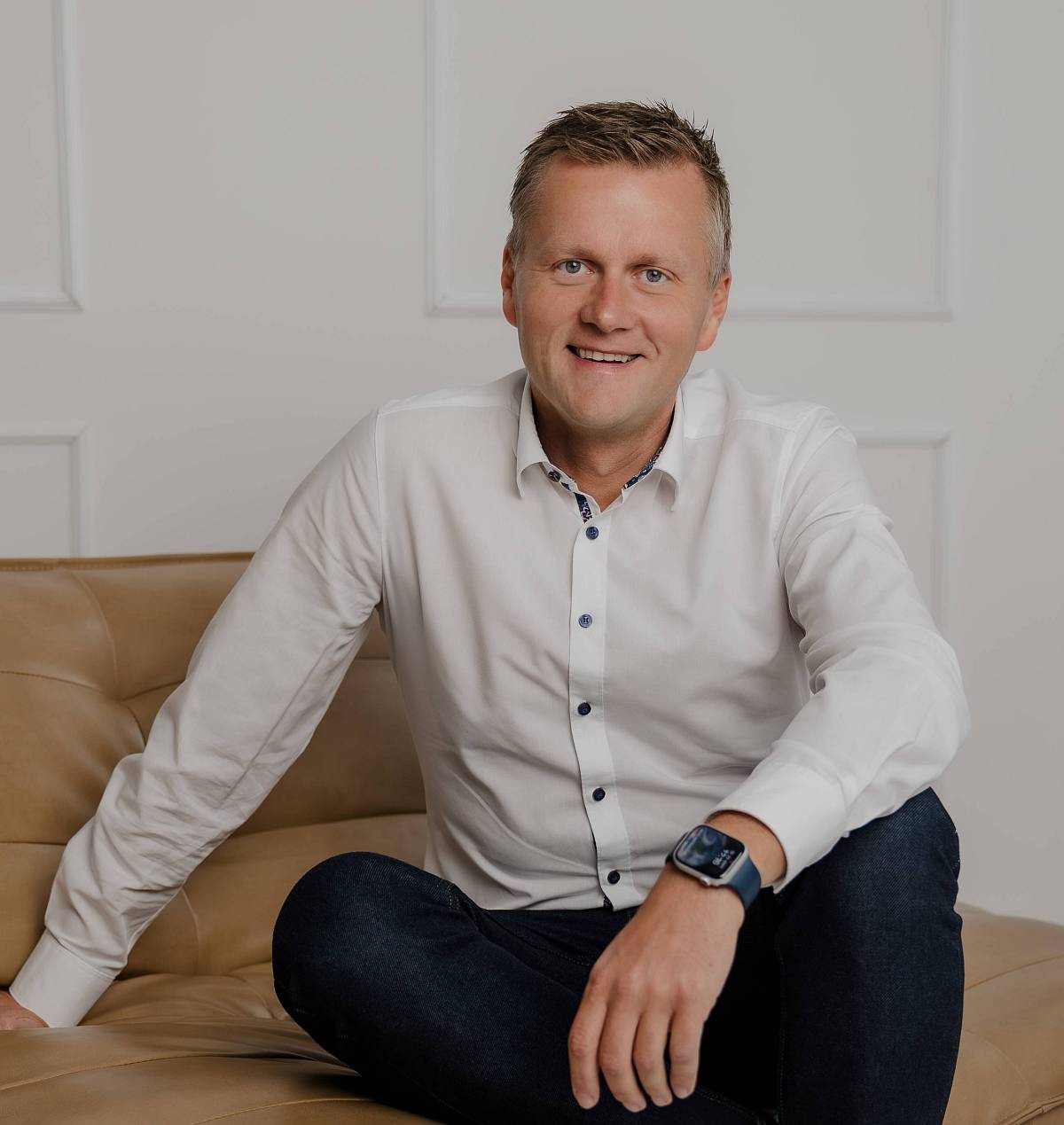 Peter Vogt sitzt entspannt auf einem Ledersofa in modernem, hellen Ambiente – ein authentisches Porträt, das Kompetenz, Vertrauen und Bodenständigkeit ausstrahlt.