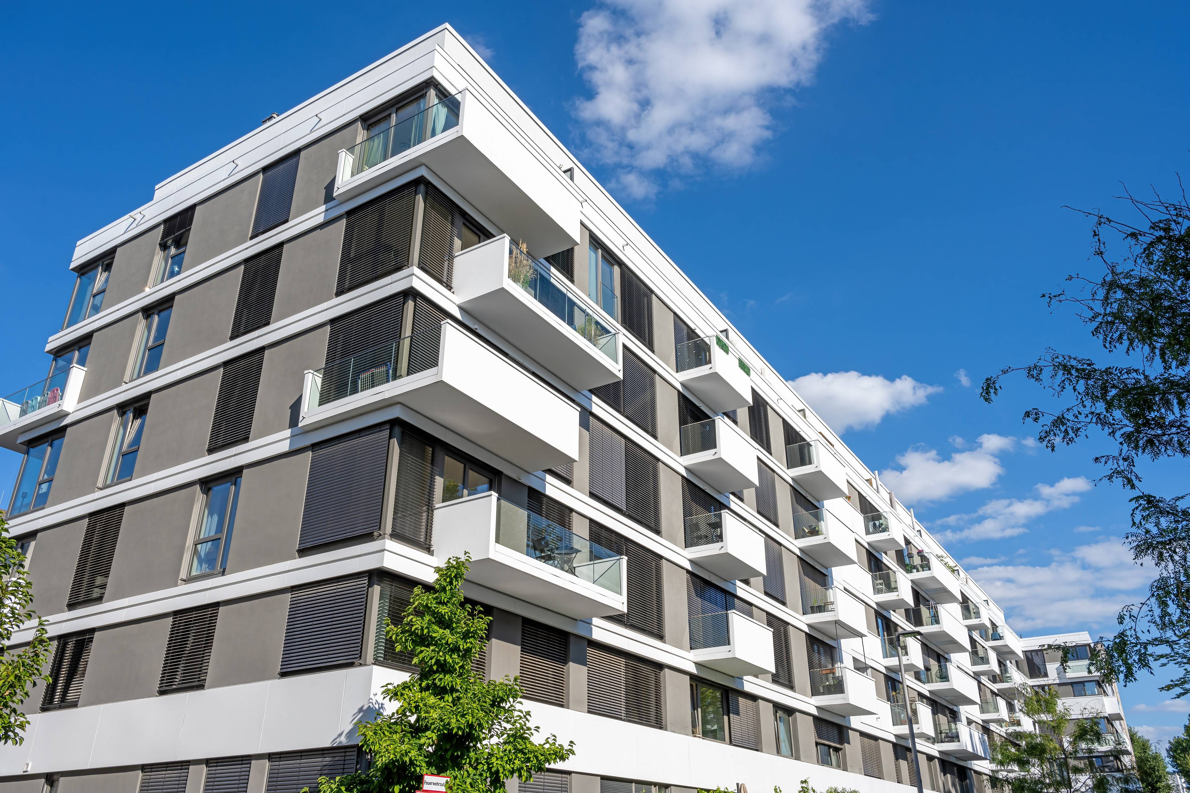 Modernes Mehrfamilienhaus mit Balkonen und klarer Architektur vor blauem Himmel – Beispiel einer erfolgreich vermittelten Immobilie.