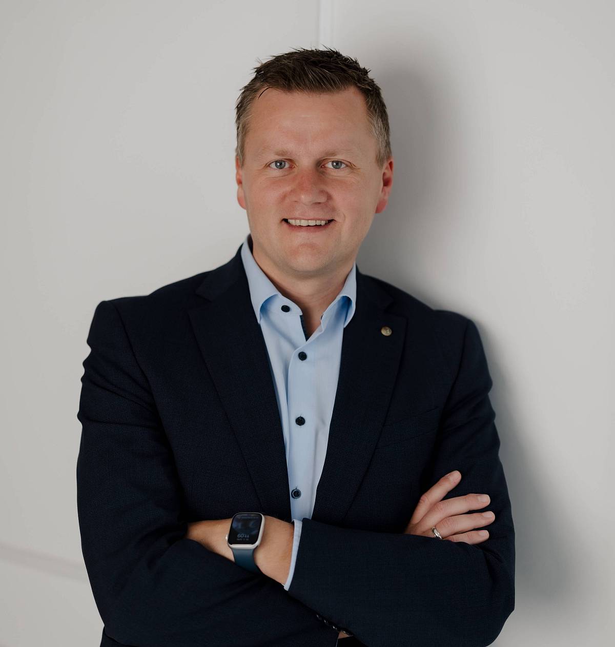 Peter Vogt in Businesskleidung vor hellem Hintergrund, lächelnd mit verschränkten Armen – professionelles Porträt für die Immobilienbranche.