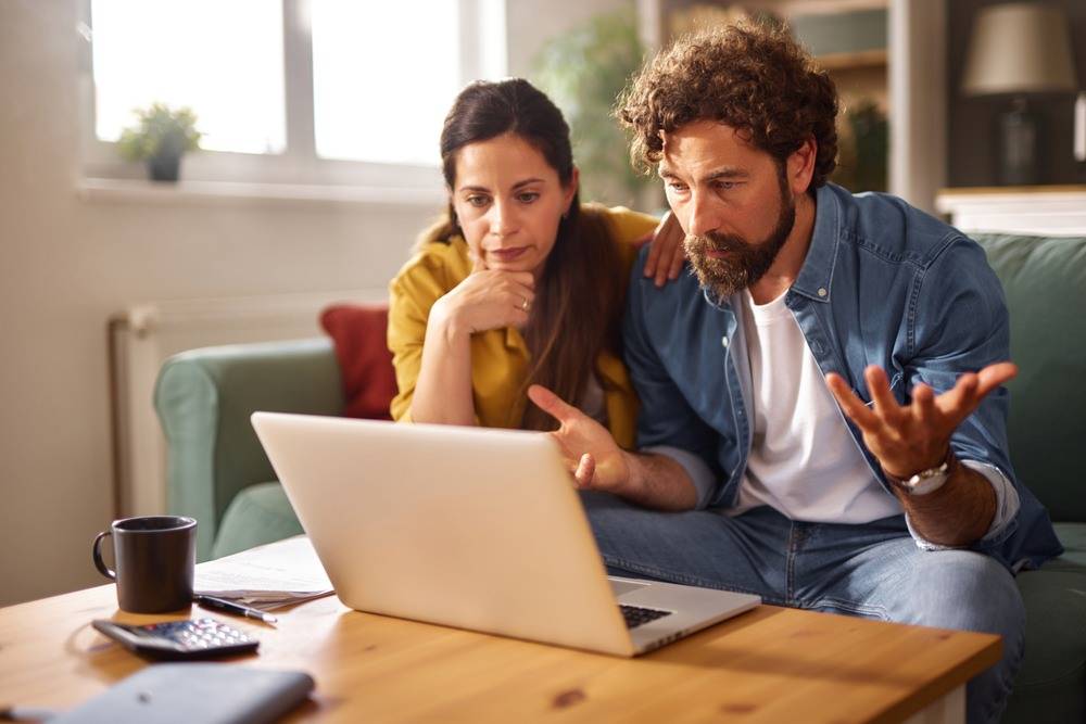 Paar sitzt am Laptop und informiert sich über ein offenes Bieterverfahren beim Verkauf eines Mehrfamilienhauses.