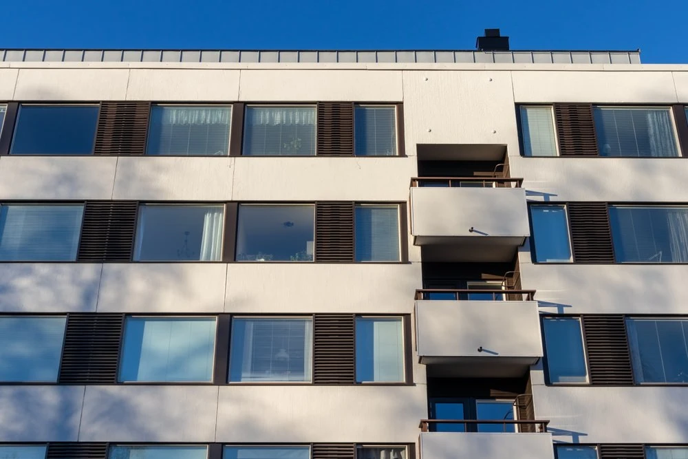 Moderne Fassade eines Mehrfamilienhauses mit Balkonen und großen Fenstern bei blauem Himmel.