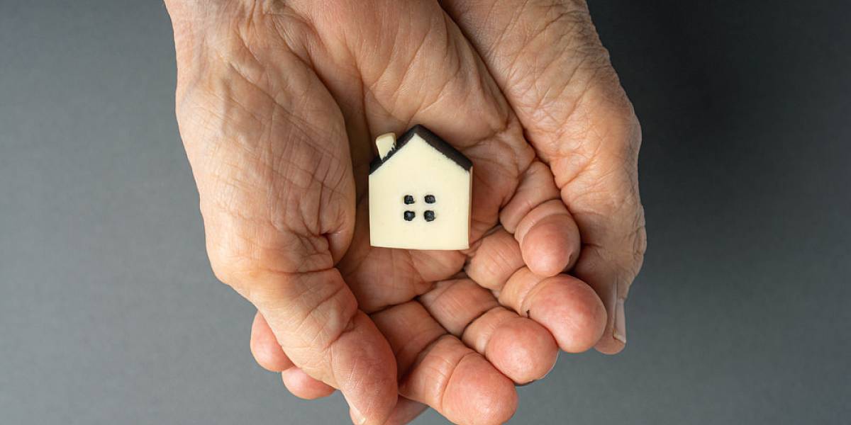 Ältere Hände halten ein Hausmodell als Symbol für Erbe, Vermögensweitergabe und langfristige Immobilienvorsorge