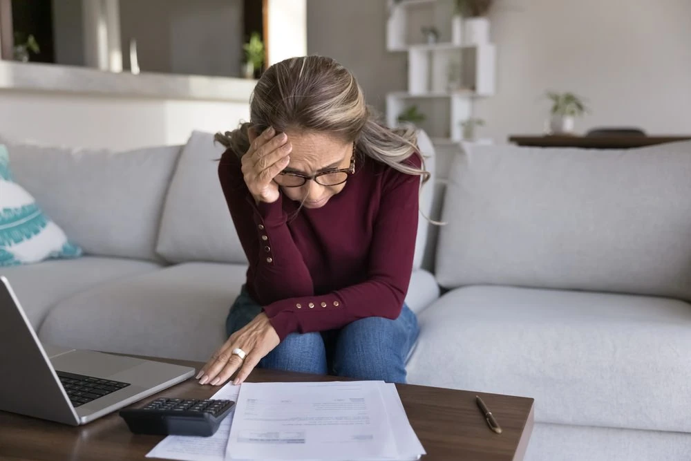 Frau prüft Rechnungen und Unterlagen mit besorgtem Blick als Symbol für finanzielle Belastung und Kostenrisiken bei Immobilien