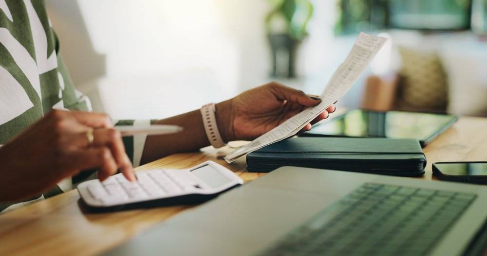 Person prüft Belege und berechnet Kosten mit Taschenrechner als Grundlage für Renditeberechnung einer Immobilie