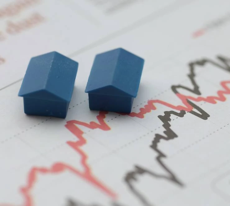 Zwei Hausmodelle auf Finanzdiagramm als Symbol für Renditeentwicklung und Marktanalyse bei Immobilieninvestitionen