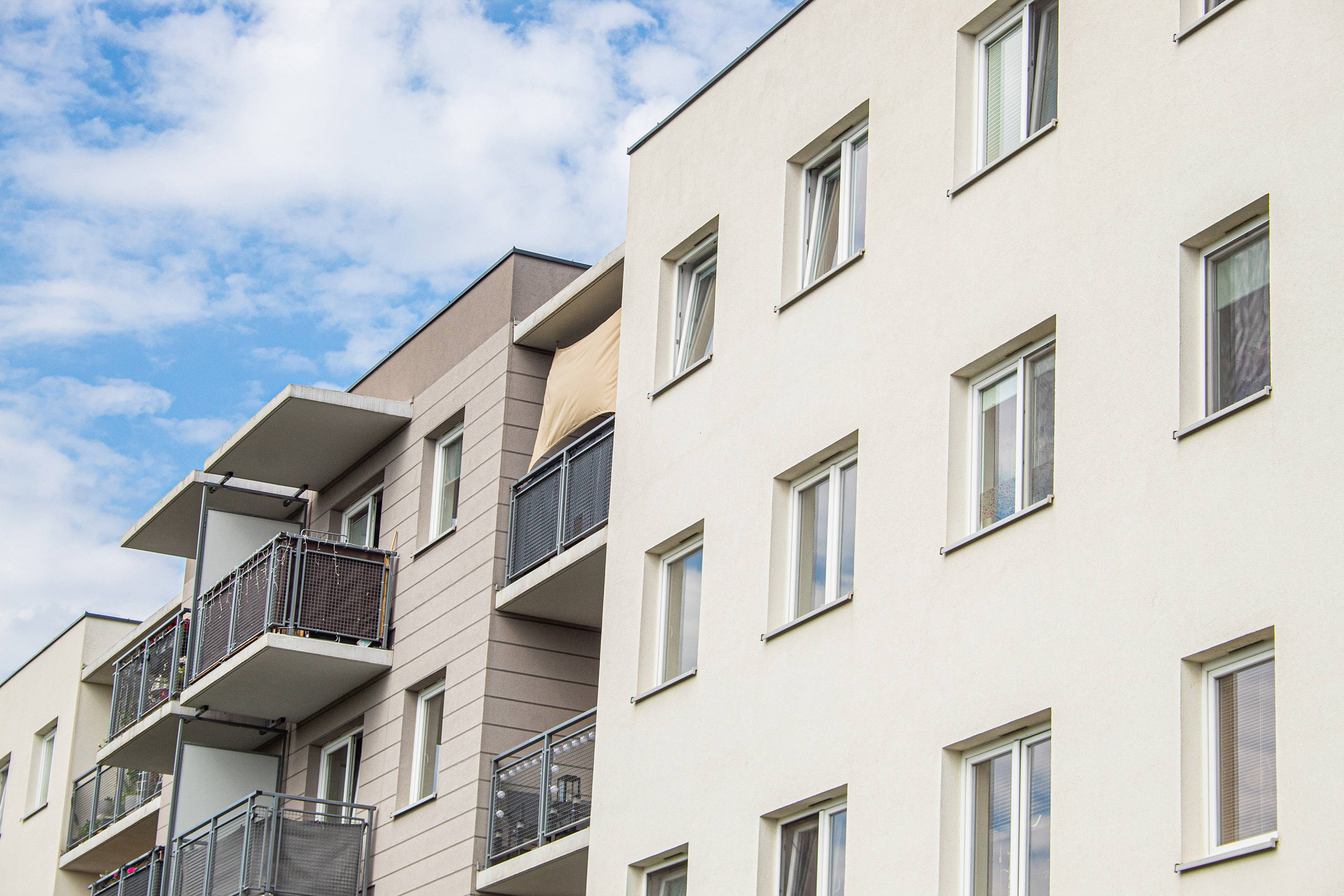 Mehrstöckiges Wohngebäude mit heller Fassade, mehreren Balkonen und großen Fenstern unter blauem Himmel.