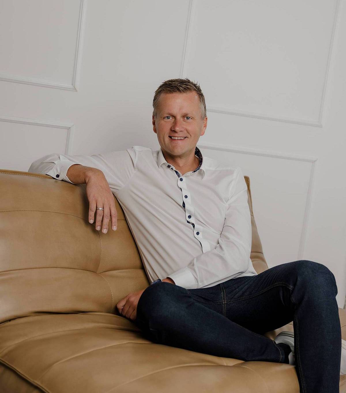 Peter Vogt sitzt entspannt auf einem Ledersofa vor einer hellen Wand und blickt lächelnd in die Kamera.