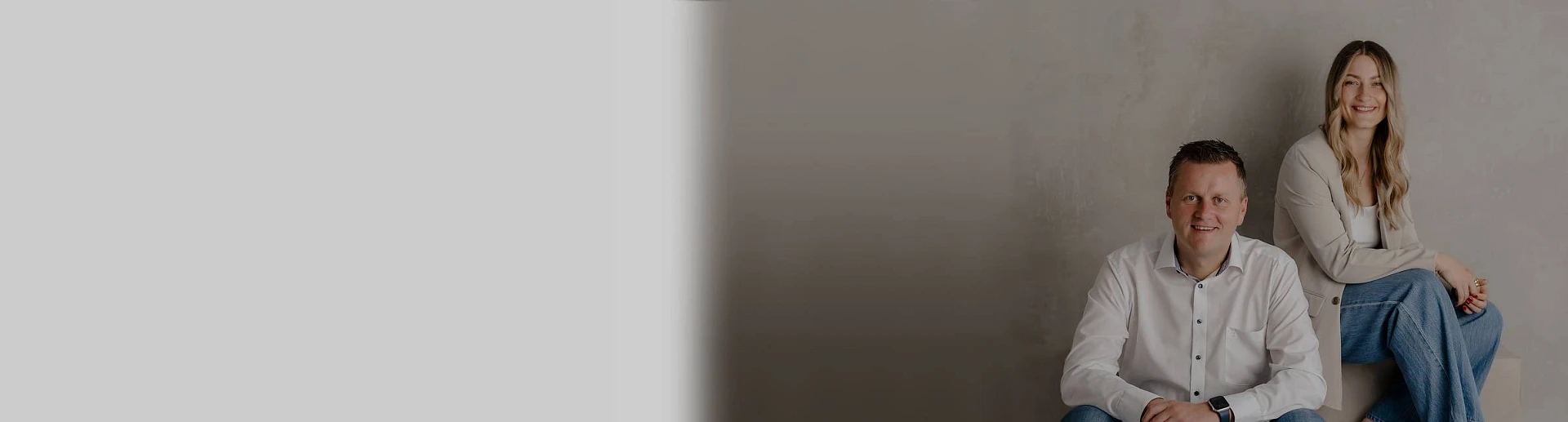 Peter Vogt sitzt gemeinsam mit einer Kollegin vor einer neutralen Wand und blickt freundlich in die Kamera.