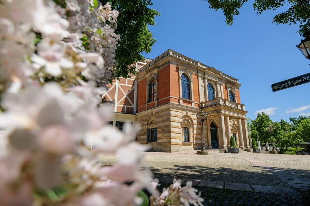 Historisches Gebäude in Bayreuth mit blühenden Bäumen und sonnigem Vorplatz