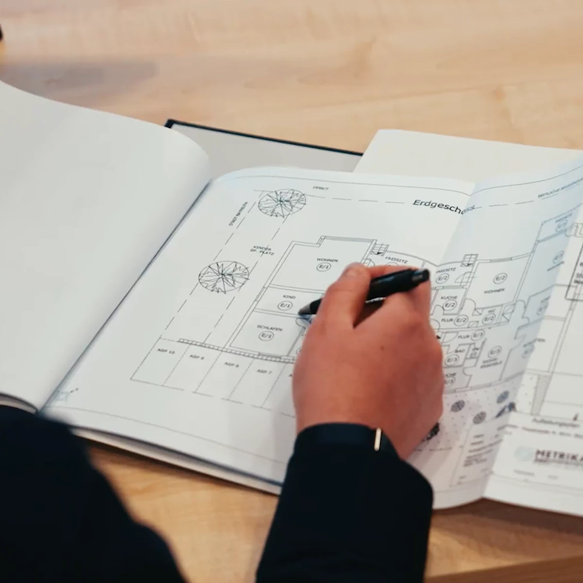 Person prüft einen Gebäudegrundriss und markiert Details auf einem Bauplan.