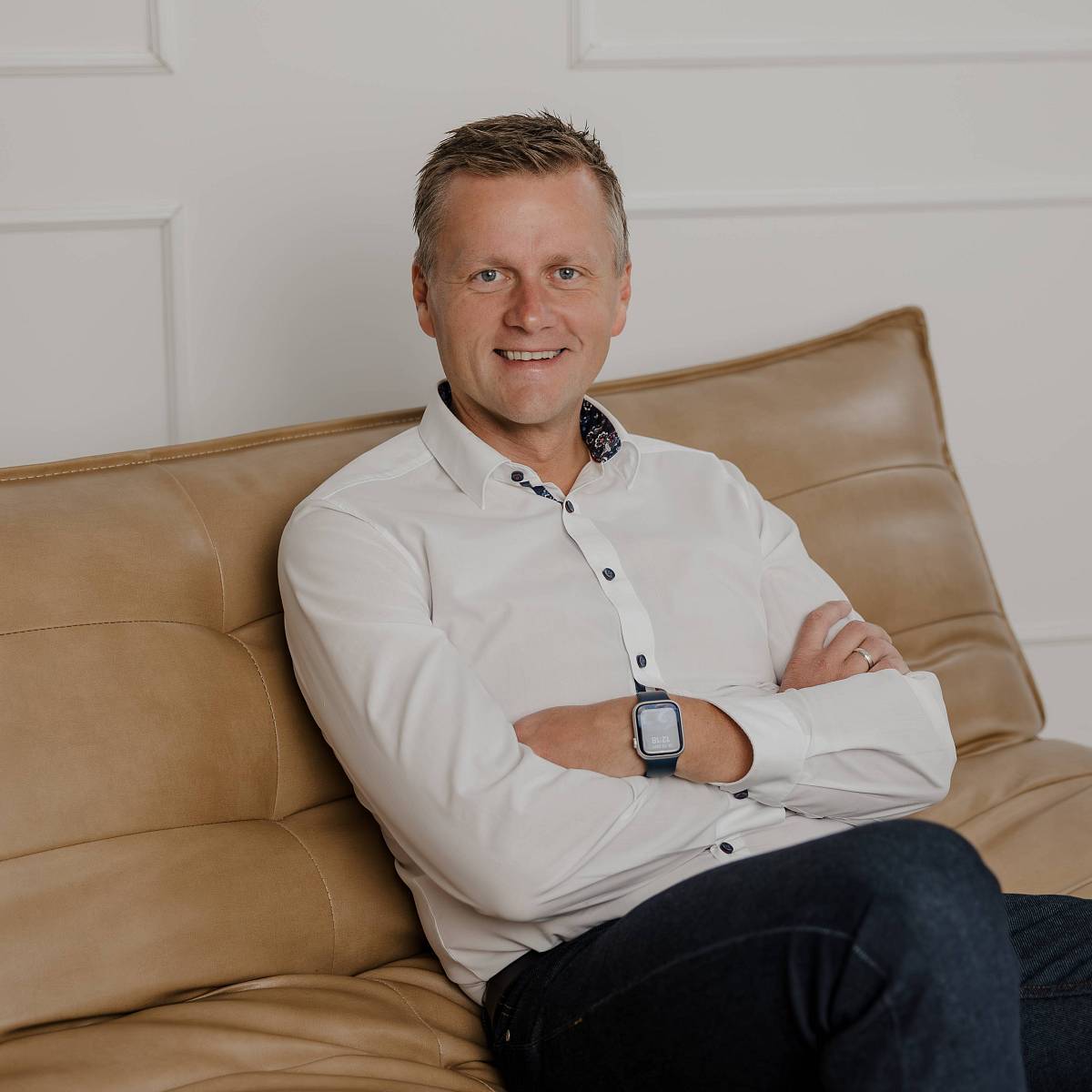 Peter Vogt sitzt entspannt auf einem Ledersofa vor einer hellen Wand und blickt lächelnd in die Kamera.