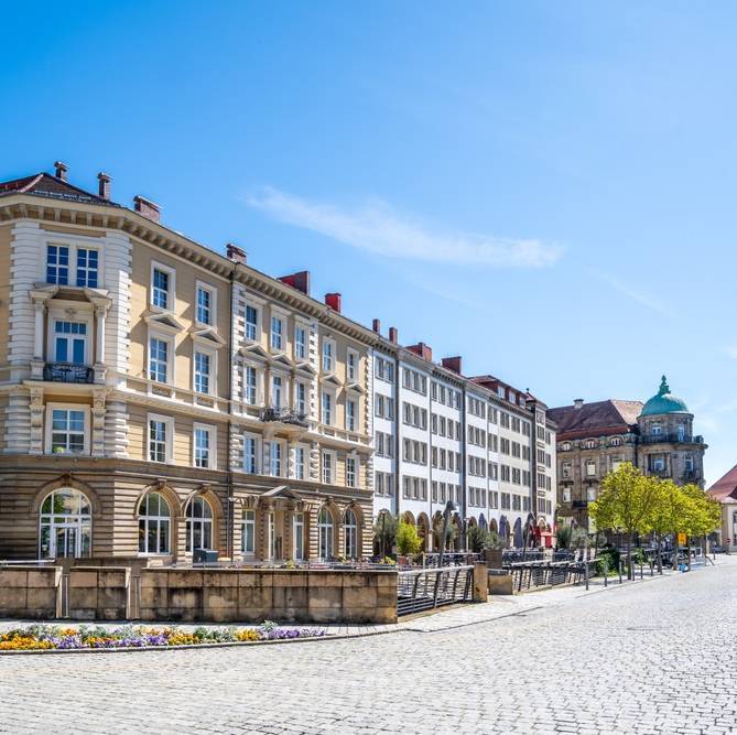 Historische Häuserzeile mit repräsentativen Fassaden an einer gepflasterten Straße in der Bayreuther Innenstadt.