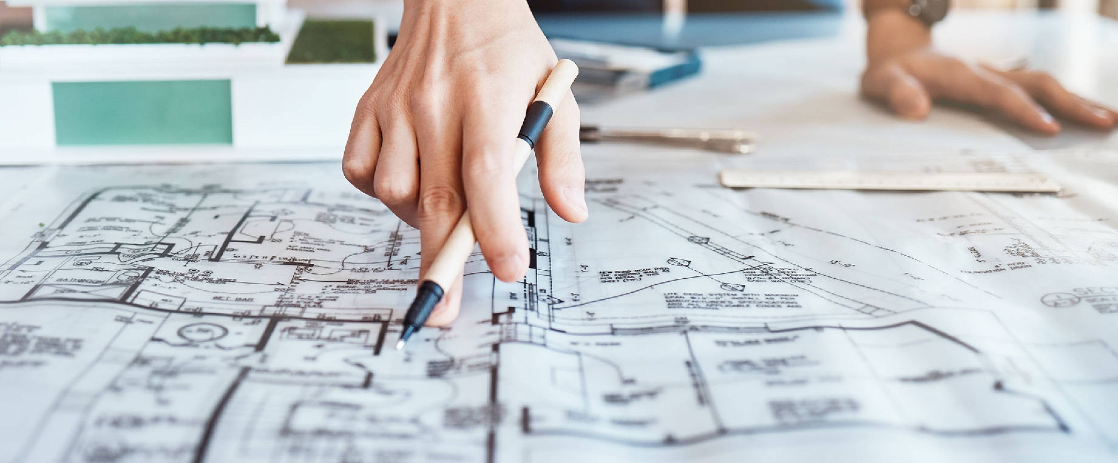 Architekt oder Planer zeigt mit Stift auf technischen Bauplan – Fokus auf Immobilienbewertung und Grundriss