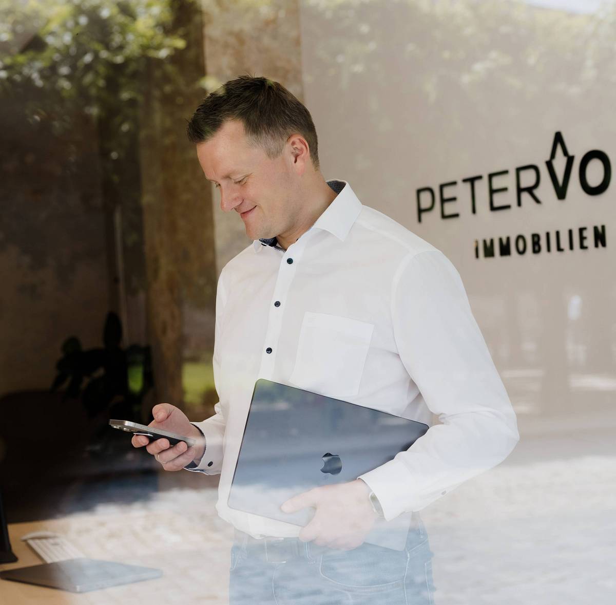 Peter Vogt steht mit Smartphone und Laptop vor dem Immobilienbüro – modernes Arbeiten und persönliche Beratung in Bayreuth.