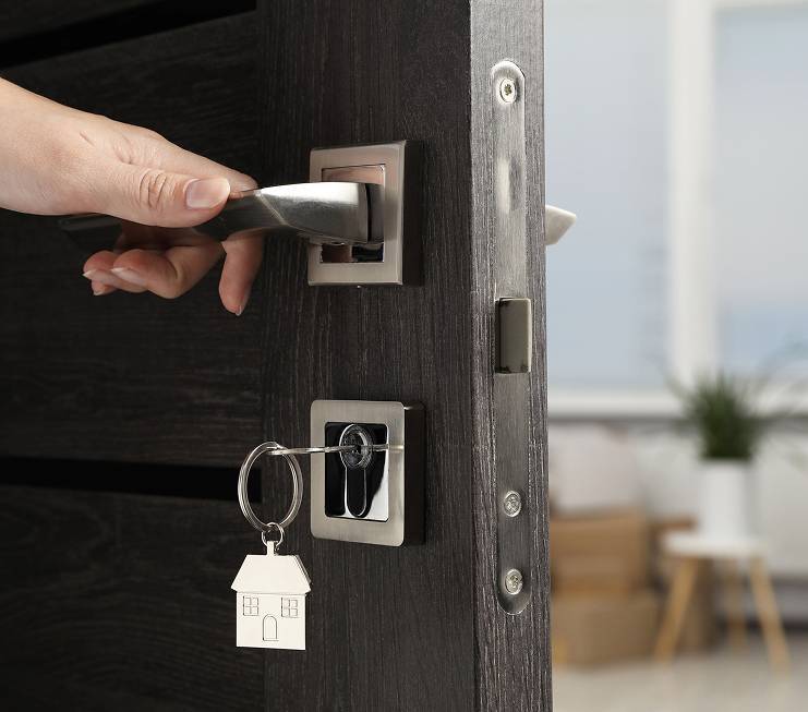 Hand öffnet eine Haustür mit Schlüssel, an dem ein Schlüsselanhänger in Form eines Hauses hängt – Symbol für diskreten Immobilienverkauf und vertrauliche Übergabe.          ChatGPT fragen