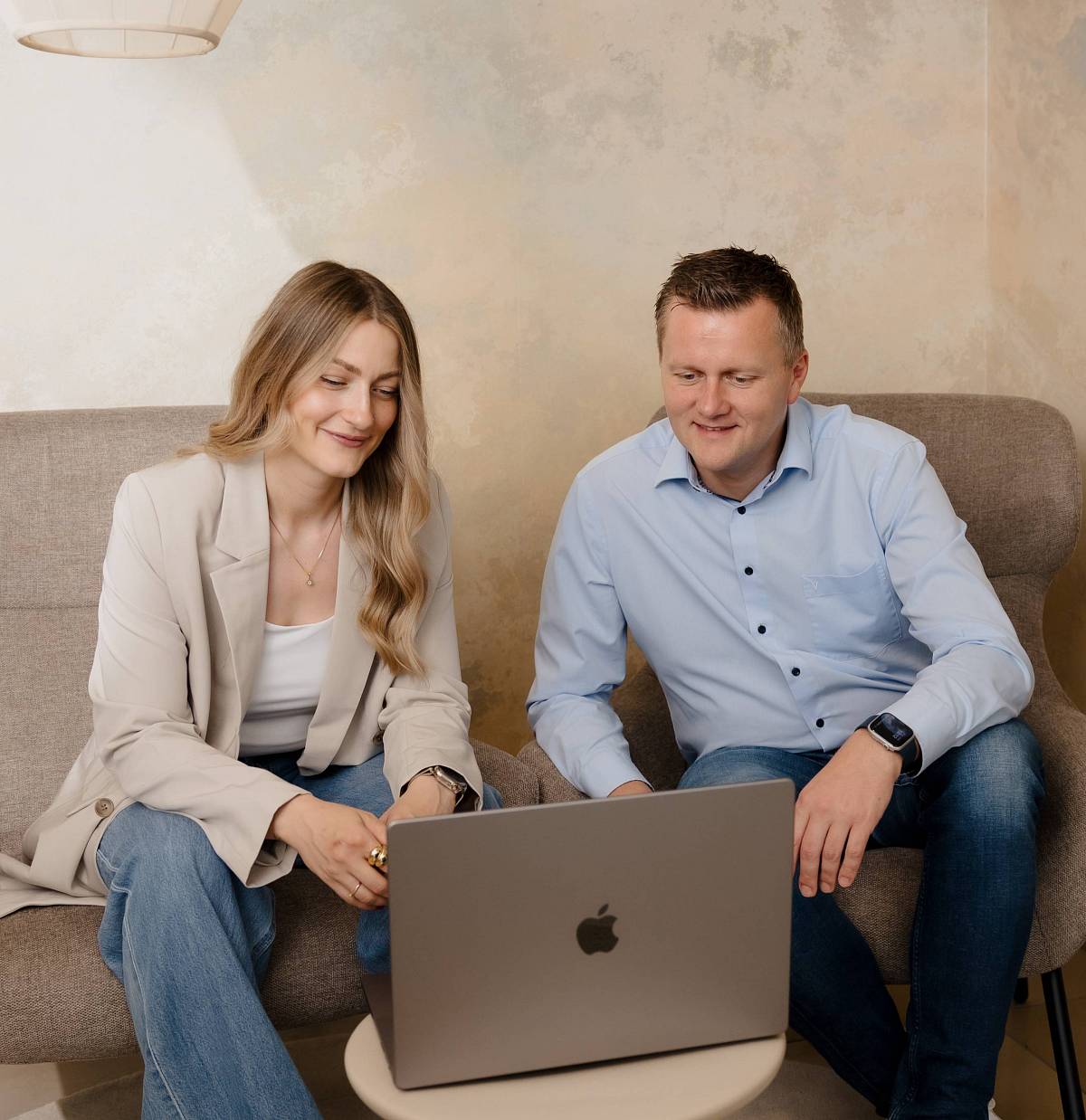 Zwei Immobilienexperten im Gespräch: Frau und Mann sitzen in modernem Büro auf Sesseln und blicken gemeinsam auf einen Laptop – symbolisiert persönliche Beratung und individuelle Betreuung beim Immobilienverkauf.