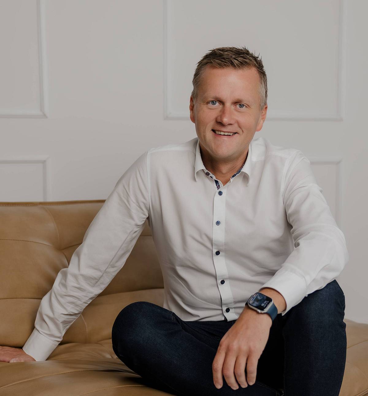 Peter Vogt sitzt entspannt auf einem Ledersofa in modernem, hellen Ambiente – ein authentisches Porträt, das Kompetenz, Vertrauen und Bodenständigkeit ausstrahlt.