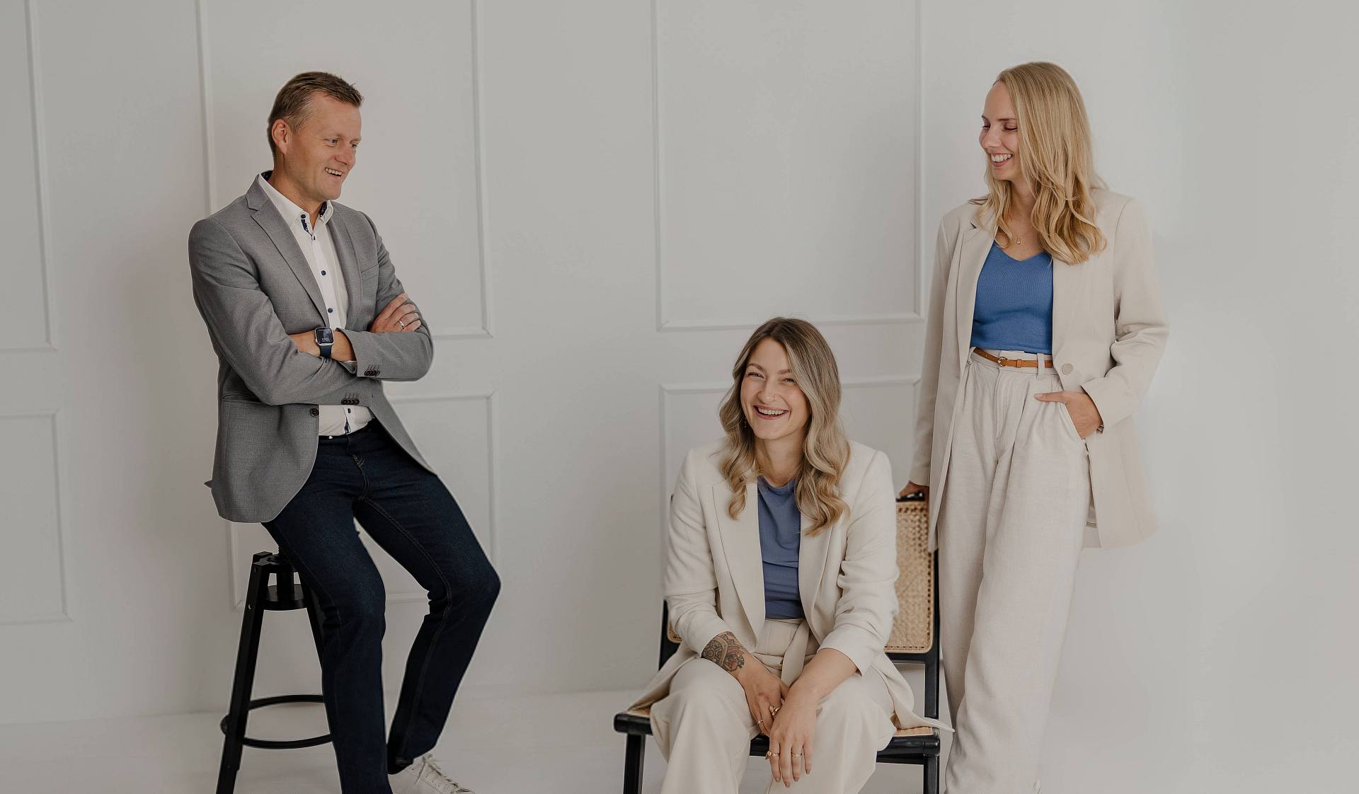 Das Bild zeigt Peter Vogt mit zwei Mitarbeiterinnen in einem hellen, minimalistischen Studio. Alle drei wirken entspannt und professionell – in neutralen, aufeinander abgestimmten Outfits mit blauen Akzenten. Das Motiv vermittelt Teamgeist, Vertrauen und die moderne, sympathische Haltung von Peter Vogt.
