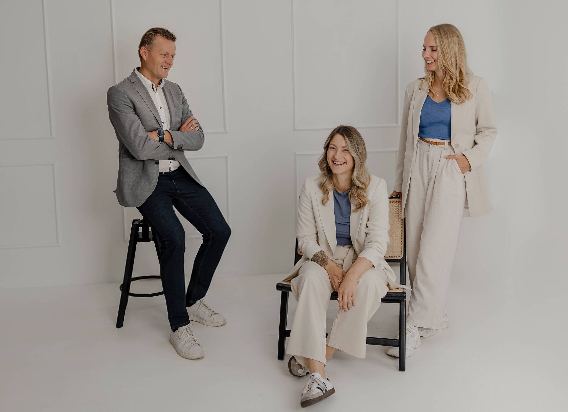 Das Bild zeigt Peter Vogt mit zwei Mitarbeiterinnen in einem hellen, minimalistischen Studio. Alle drei wirken entspannt und professionell – in neutralen, aufeinander abgestimmten Outfits mit blauen Akzenten. Das Motiv vermittelt Teamgeist, Vertrauen und die moderne, sympathische Haltung von Peter Vogt.