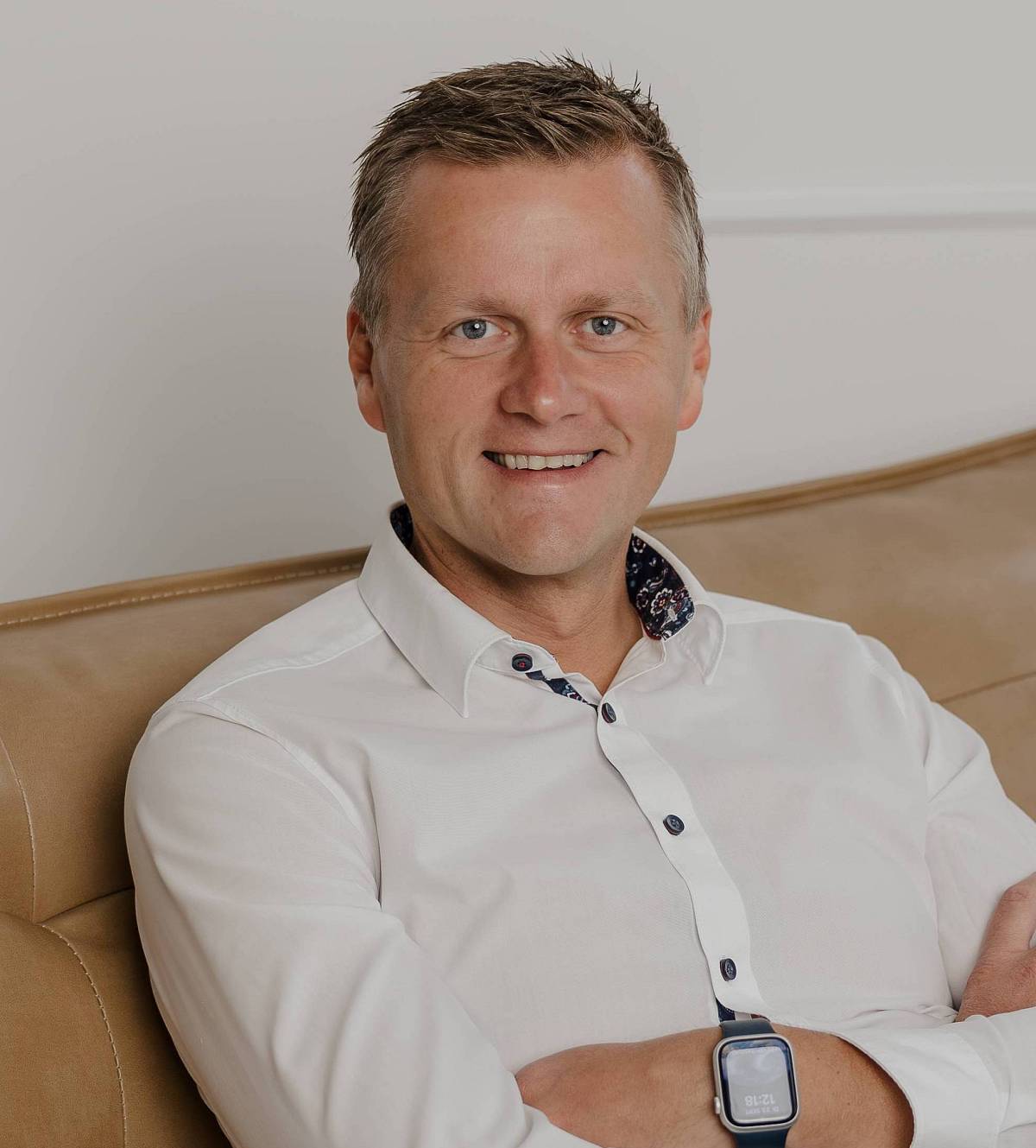 Das Bild zeigt Peter Vogt entspannt auf einem beigen Ledersofa. Mit offenem Lächeln, weißem Hemd und moderner Uhr vermittelt er Vertrauen, Kompetenz und Bodenständigkeit – ein authentisches Porträt, das seine Professionalität und Nahbarkeit unterstreicht.