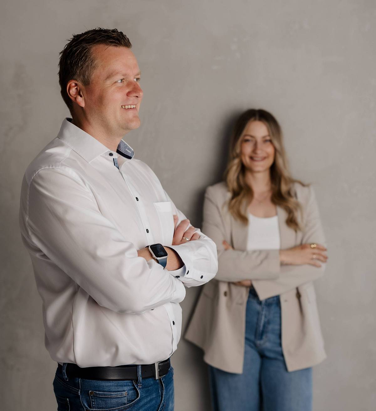 Peter Vogt und Lejla von Peter Vogt Immobilien stehen entspannt vor einer grauen Wand und blicken selbstbewusst in die Zukunft.