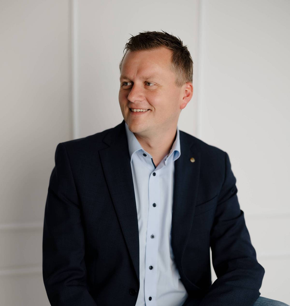 Peter Vogt, Immobilienexperte, im Business-Outfit lächelnd sitzend vor hellem Hintergrund