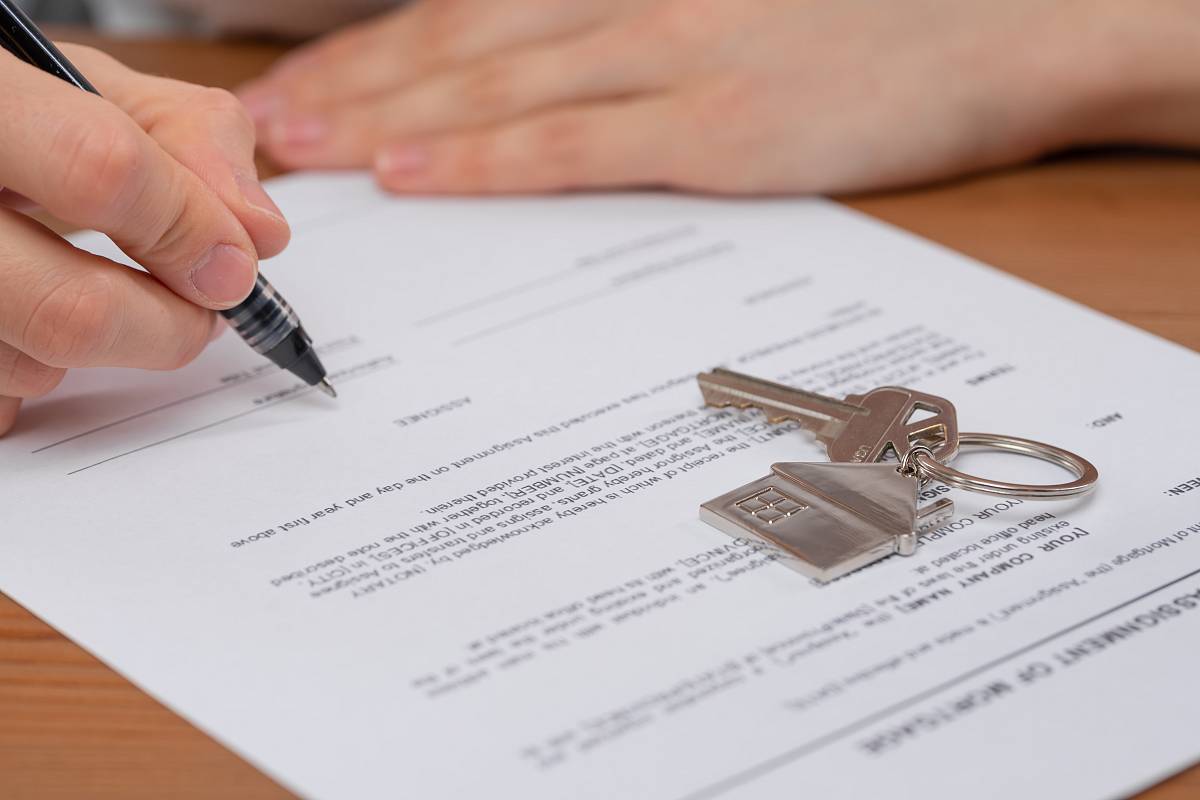 Hand unterzeichnet einen Immobilienkaufvertrag, daneben ein Schlüsselbund – Vertragsabschluss beim Immobilienkauf.
