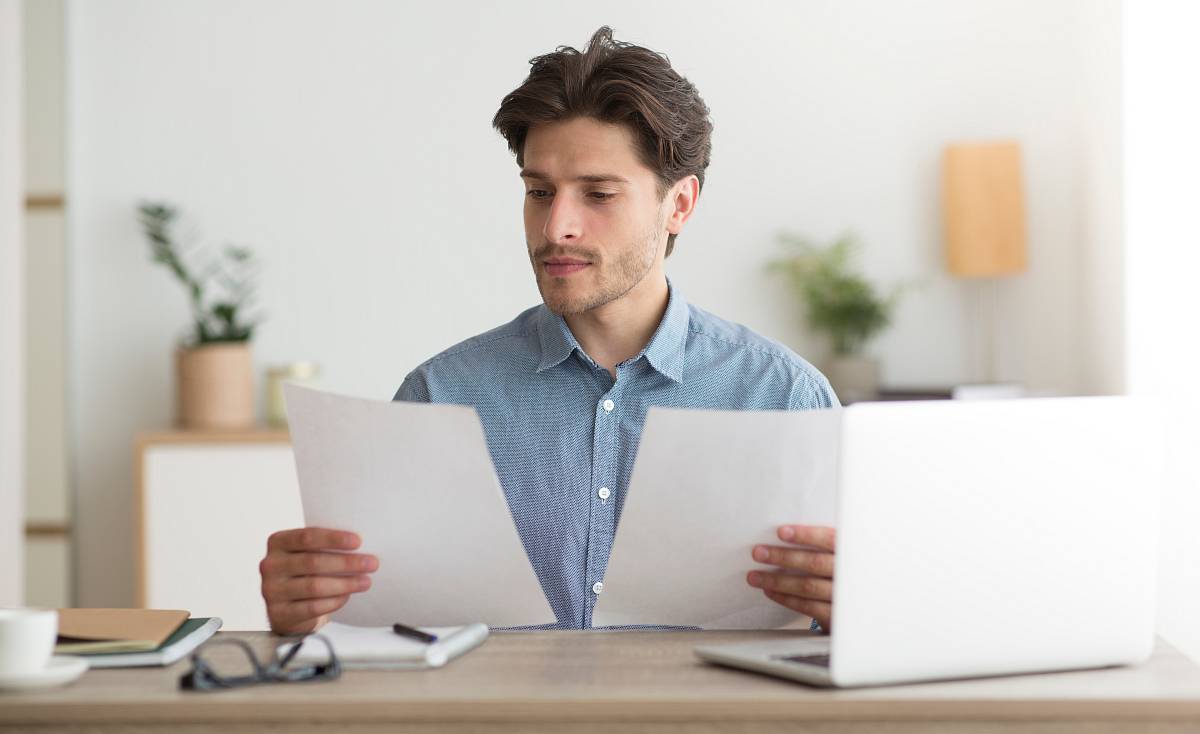 Mann prüft konzentriert Unterlagen am Schreibtisch – Dokumentenprüfung vor einem Immobilienverkauf.